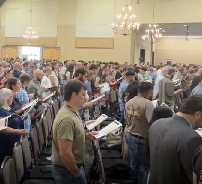 Hundreds of Christians singing together from hymnals at the New Christendom Press conference